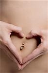 Close-up of a young woman forming heart shape with her fingers on her belly button