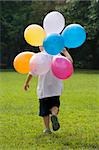 Rear view of a boy holding balloons and running in a playground