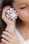 Close-up of a girl holding a spiral seashell close to her ear