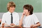 Two schoolboys looking at each other and smiling in a classroom