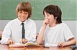 Two schoolboys reading a book together in a classroom and smiling