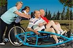 Two senior men sitting on a quadracycle and two senior women pushing it