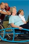 Two senior women sitting on a quadracycle and two senior men pushing it