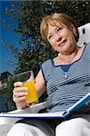 Low angle view of a senior woman sitting on a chair and drinking juice