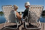 Rückansicht des ein altes Paar, sitzen auf Stühlen am Seeufer