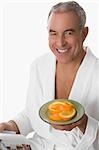 Portrait of a senior man holding a plate of orange and smiling