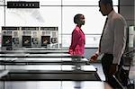 Side profile of a businessman checking his ticket into a check-in machine with a businesswoman standing beside him