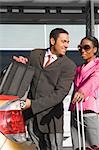 Businessman loading his suitcase on a car trunk with a businesswoman standing beside him