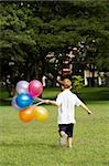 Vue arrière d'un garçon tenant des ballons dans un parc