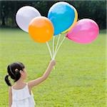 Rear view of a girl holding balloons in a park