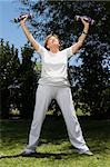 Senior woman exercising with dumbbells in a garden