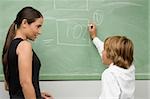 Schoolboy writing on a blackboard and his teacher looking at him