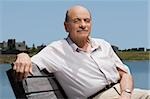 Portrait d'un homme senior assis sur un banc au bord du lac