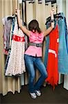 Young woman holding dresses in a fitting room and posing