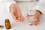 A young woman's hand holding a glass of water and pills
