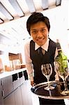 Waiter carrying bottle of wine and glasses on tray
