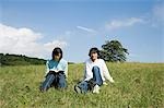 Young couple sitting on field, woman reading book