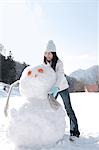 Young woman putting scarf on snowman