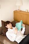 Young woman reading book lying on sofa