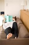 Young woman reading book lying on sofa