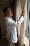 Mature man opening curtain in hotel room