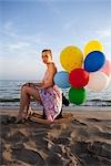 Woman With Colourful Balloons Sitting on a Rocking Horse on the Beach