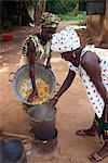Two women in traditional clothing, cooking soup in a bucket over a small fire outdoors, Gambia, West Africa, Africa