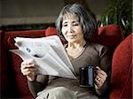 senior woman reading a newspaper on the couch