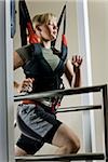 young woman running on a treadmill in a harness