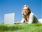 woman lying on the grass using a laptop