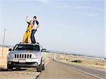 couple on the roof of their car on the side of the road