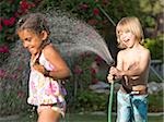 little boy spraying a little girl with the hose