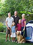 family standing in their backyard with a tent and their dog