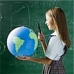 girl in a classroom standing in front of a chalkboard looking at a globe with a magnifying glass