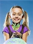 girl looking at the camera holding a plant in front of a globe