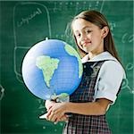 girl in a classroom standing in front of a chalkboard holding a globe