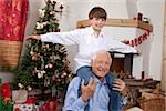 Grandfather carrying boy on shoulders at Christmas tree