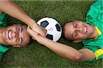 Two Brazilian kickers lying on grass, holding hands