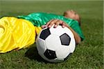 Exhausted Brazilian soccer player lying on grass, hand resting on ball