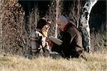 Mann und Frau sitzen vor einem Holz, in einem Buch lesen