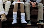 Three Friends sitting next to each other with their Hands folded in their Laps - Wooden Footbridge - Warm Clothing - Season