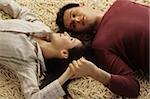 Jeune homme couché tête à tête avec sa petite amie sur un tapis, tenant de sa main - relation - amour - Accueil - salon