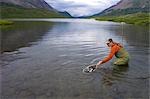 Fly fisherwoman nets wild Arctic grayling in Landmark Gap Lake a large alpine lake in the Alaska Range Alaska southcentral summer