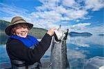 Teenage boy standing in a boat holding a silver salmon that he caught in Prince William Sound, Southcentral, Alaska