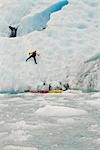 Man ice climbs onto Bear Glacier in Kenai Fjords National Park after exiting his sea kayak