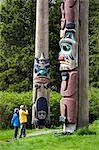 Tourist photographing totem pole at Saxman Totem Park near Ketchikan Alaska Southeast Summer