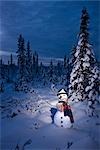 Snowman with colorful scarf and vest wearing a black top hat standing in snow covered spruce forest near Fairbanks, Alaska in Winter