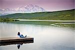 Mature couple canoes on Wonder Lake as middle age woman watches from dock with Mt. Mckinley in the background, Denali National Park, Alaska