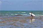 Man carrying surfboard at Praia do Forte,Bahia,Brazil