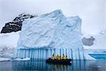 Menschen im Schlauchboot durch Eisberg, Antarktis